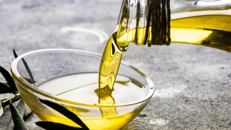 Olive oil being poured from a bottle into a glass bowl.
