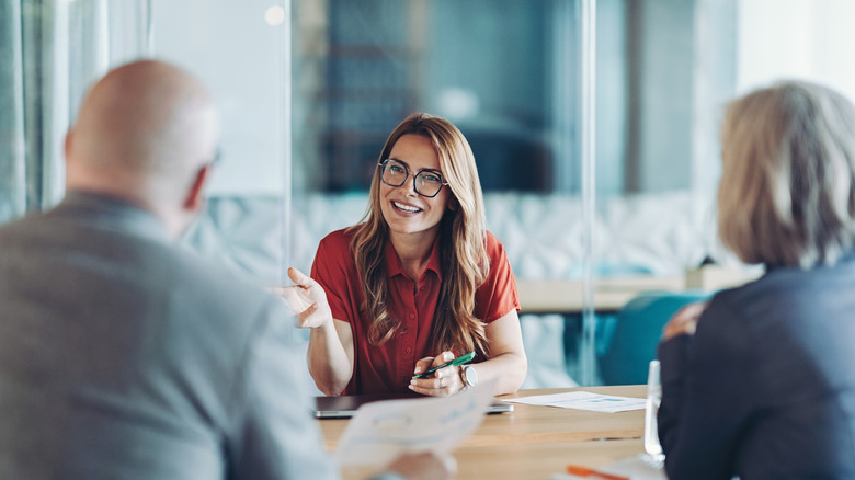 A woman in a red shirt discussing something with two older individuals facing her from across a table