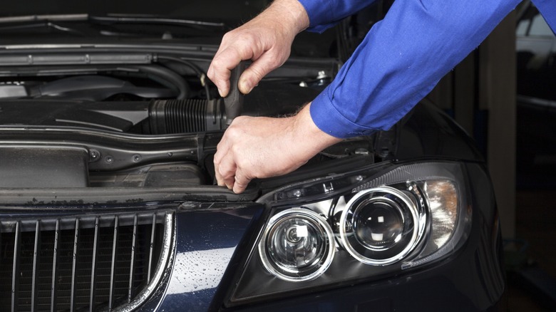 Mechanic using a screwdriver under the hood of a BMW, working near the front headlight and engine components