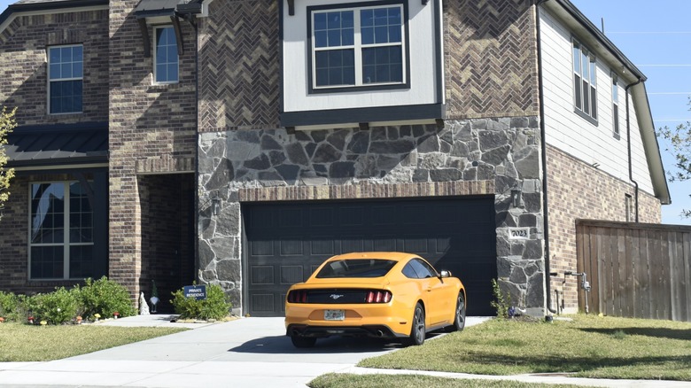 Orange Ford Mustang parked in the driveway of a two-story suburban home