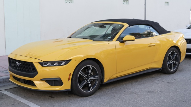 Yellow Ford Mustang convertible with black soft top parked curbside, shown from front three-quarter angle