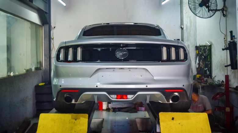Rear view of a silver Ford Mustang raised on a lift inside an auto repair shop, with tools and equipment visible around it