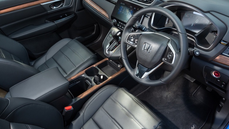 Interior view of a Honda CR-V showing black leather seats, steering wheel, center console with cupholders, and infotainment screen