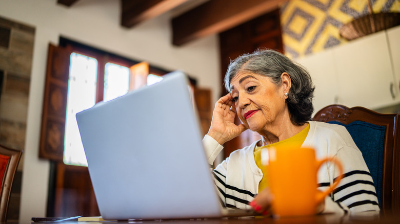 older woman looking concerned while checking her laptop in a house