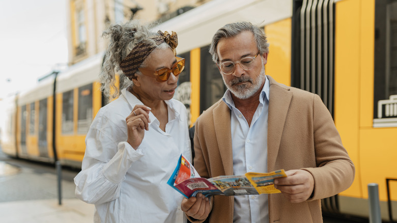 A senior couple looking underwhelmed as they examine a map in front of a train