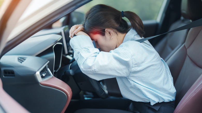 A stressed out young woman presses her head again a car steering wheel