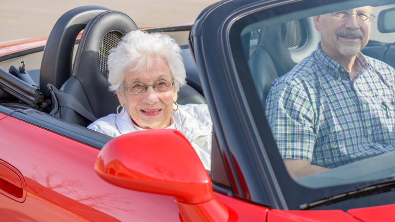 Older couple riding in a red convertible with the top down