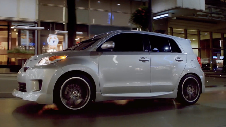 A black Scion xD parked near trees pictured from the rear.