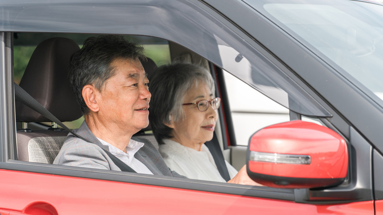 An elderly couple riding in a red car