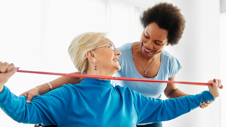 A smiling physiotherapist helping a smiling mature woman do exercises.
