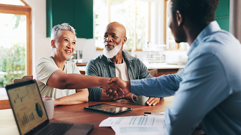 A mature couple shaking hands with their accountant at their dining room table.