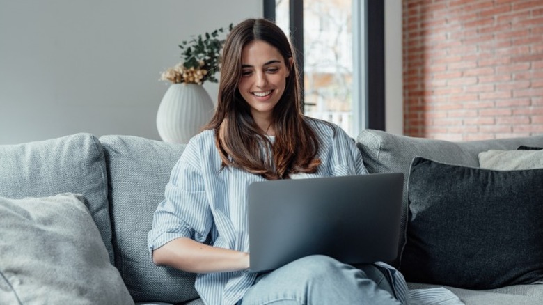A young woman smiling at a laptop while sitting on a couch
