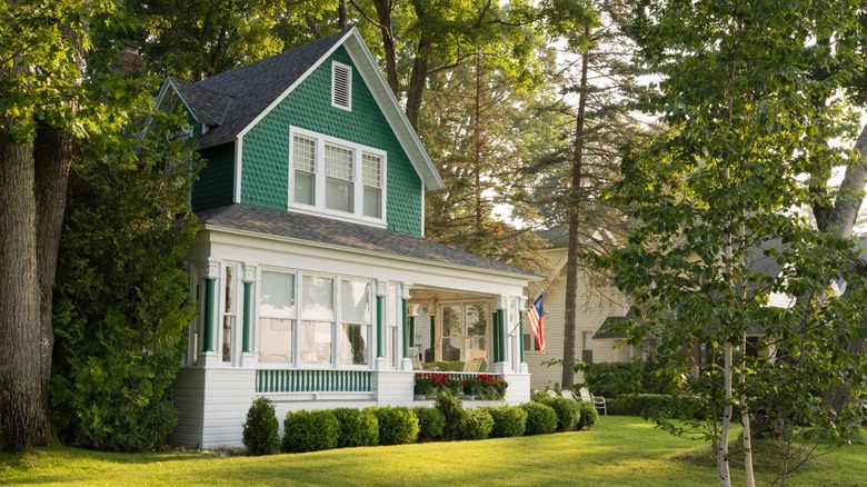A single-family house with an American flag on it surrounded by a green yard and trees