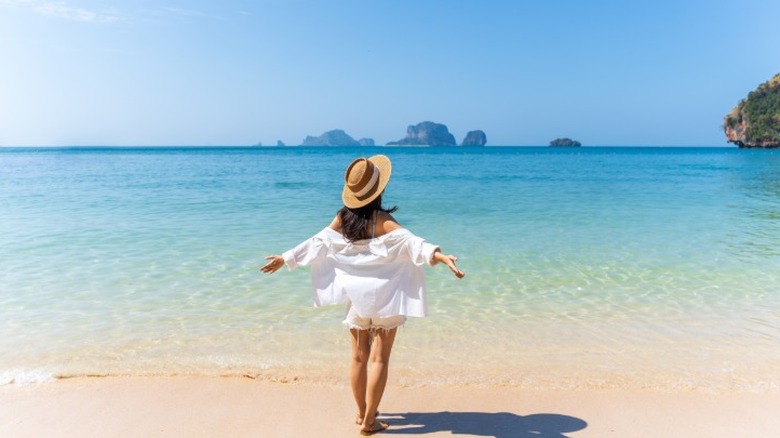 A woman on vacation standing at the wate's edge on a tropical beach