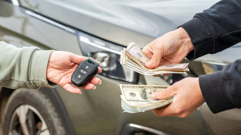 People exchanging car keys for cash with a car in background.