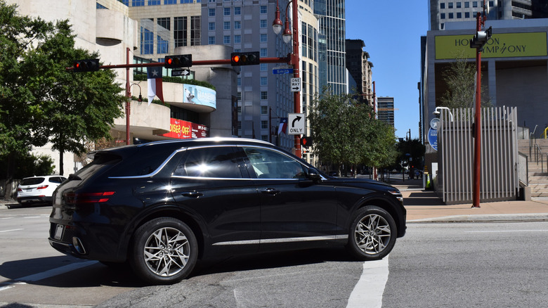 A Genesis GV70 making a turn at an intersection in a city.