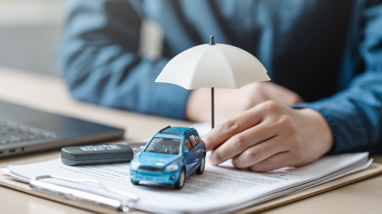 Person holding an umbrella over car figurine placed on top of a stack of documents