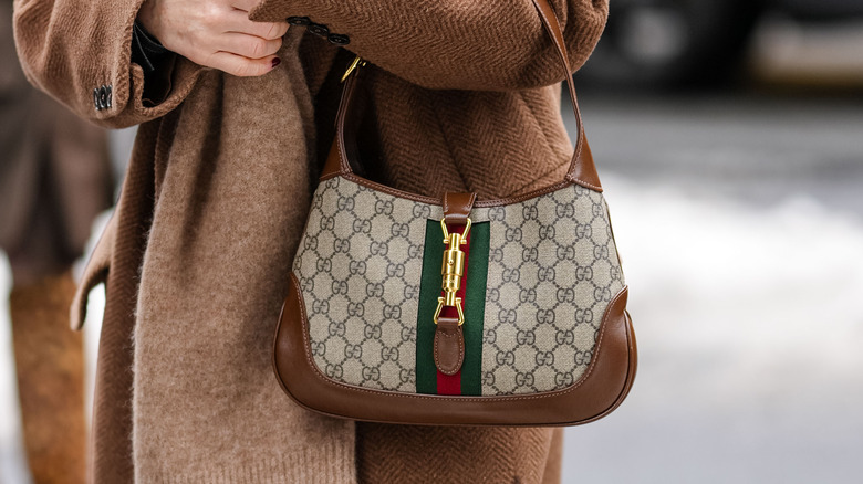 Woman wearing winter clothes crosses street holding Jackie Gucci 1961 bag