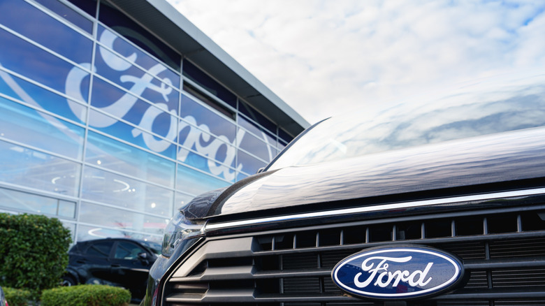 Close-up of Ford logo on a car parked in front of a Ford dealership