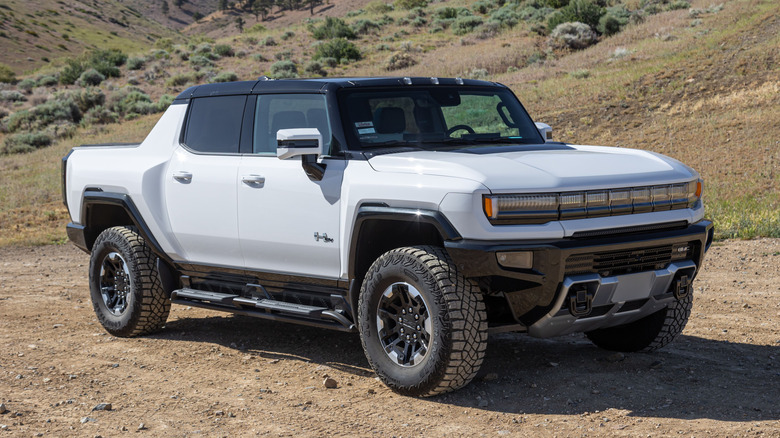 A GMC Hummer EV Pickup in white sits atop a dirt road in the rural backcountry hills.