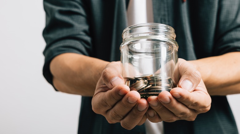 Close-up of hands of man holding out a jar full of coins