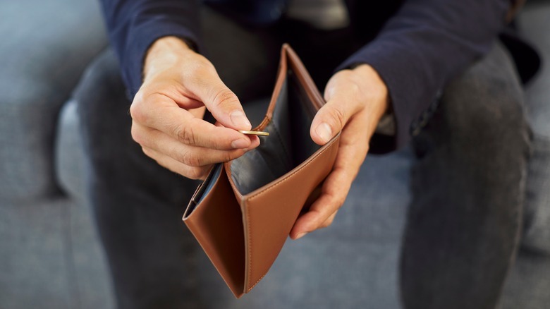 Hands of man holding a coin over an empty wallet