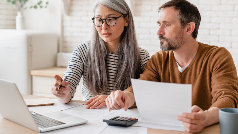 Mature couple stares at laptop screen while man holds paper