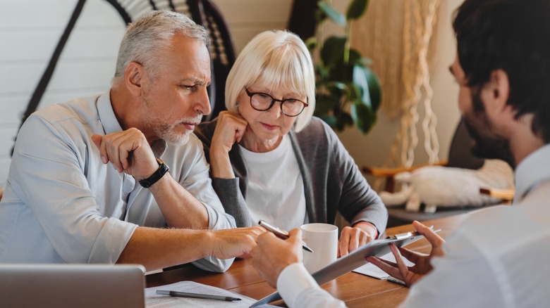 Older couple examine paper on clipboard shown to them by younger man