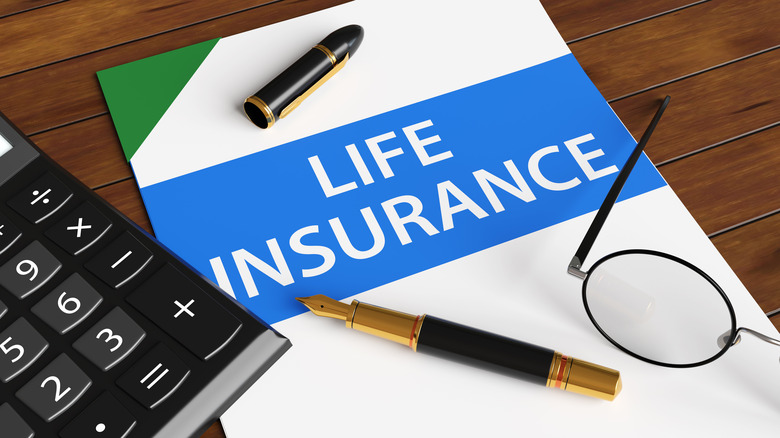 Paper with words life insurance sits under a pen, calculator, and pair of glasses