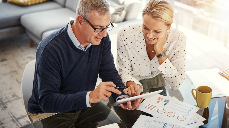 Mature happy couple looking at tablet on table with coffee cup and papers
