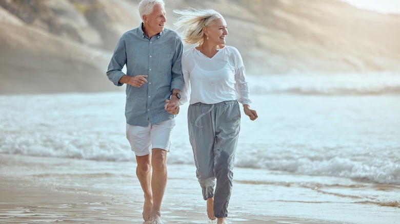 Mature couple holding hands looking to the right as they walk along a beach
