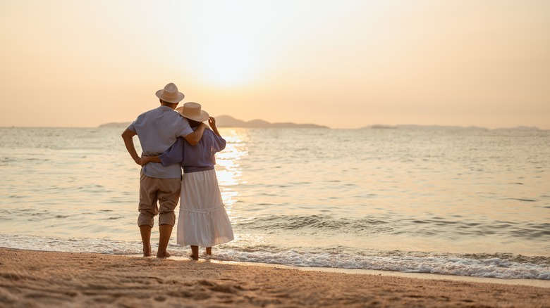 older couple standing on beach watching sunset
