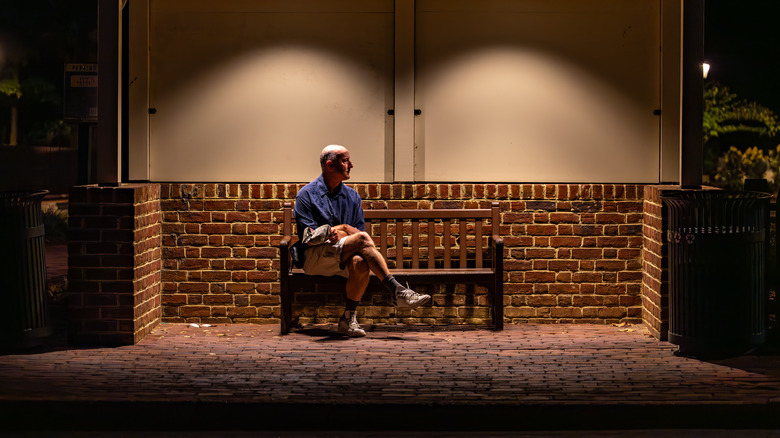 A man sits at bus stop at night with a bench in the old Colonial Williamsburg, Virginia district.