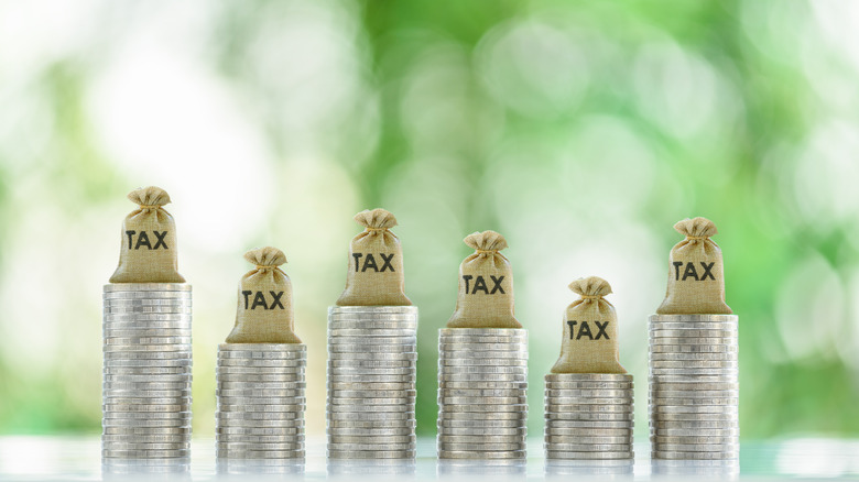 Tax bags rest atop coin stacks, depicting mandatory financial charge.