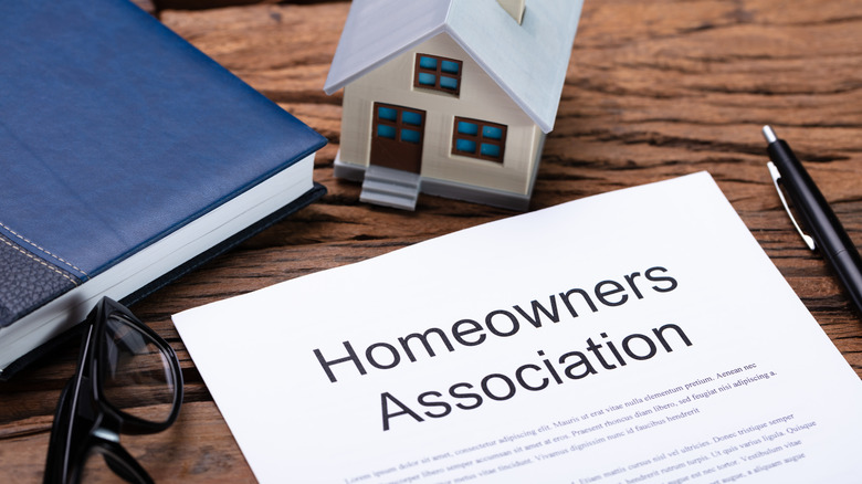 A model of a house on a desk next to a paper with HOA rules and regulations.