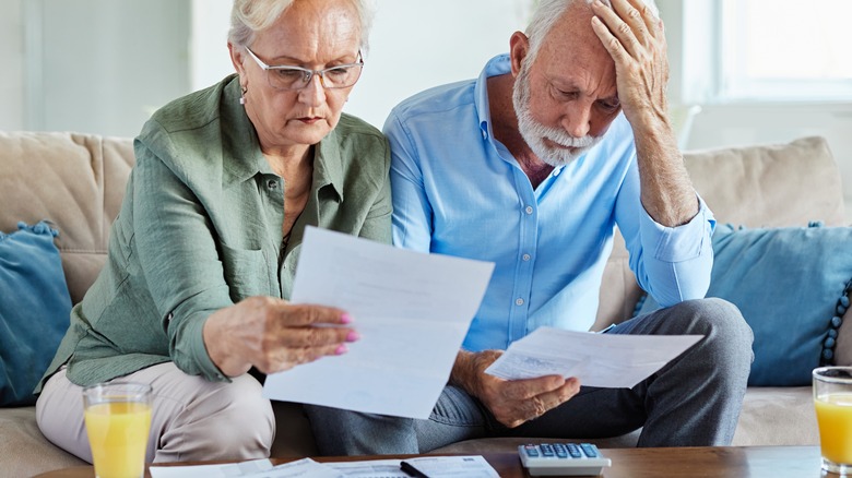 Seated elderly couple look worried as they read documents
