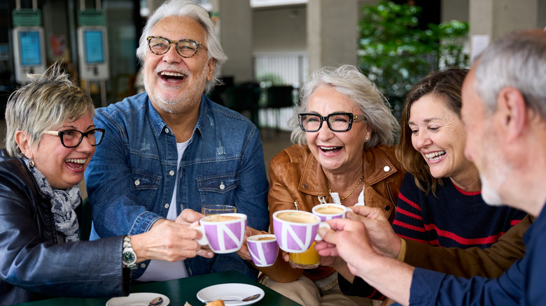 Group of mature and fashionable seniors joyously toast with hot cocoa mugs