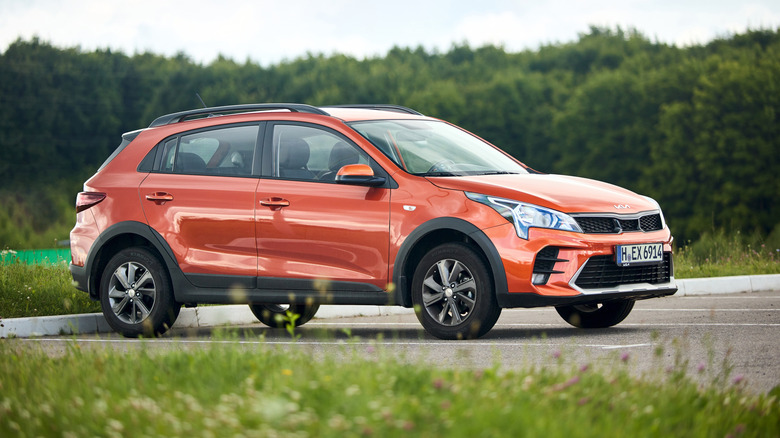 Kia Rio X 2021-2022 X-Line Burnt Orange parked in parking with forest and grass in background.