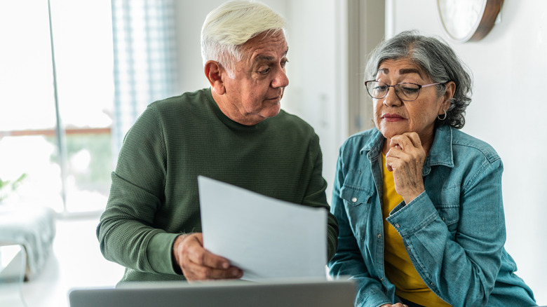 Older man holding document sits with mature woman as she looks at the page