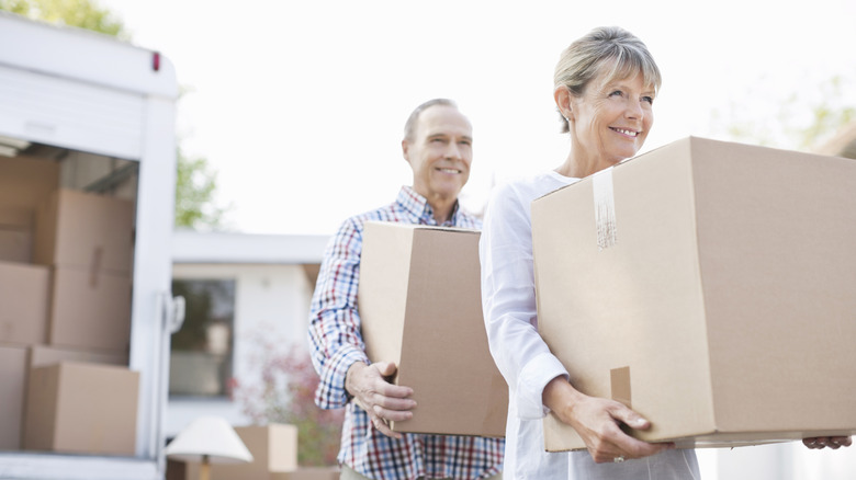 A smiling older couple carrying moving boxes