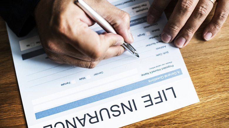Close up of man's hands as he fills out blank life insurance form