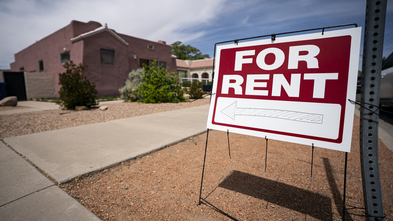 Close up of "For rent" sign with drawn arrow pointing left in front of a home