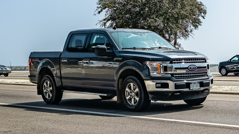 Black Ford F-150 driving down the road.