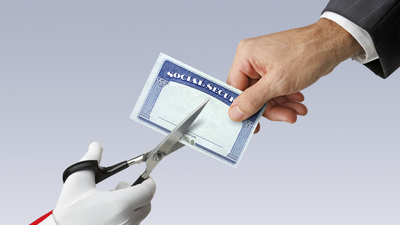 A gloved hand cutting a Social Security card with scizzors