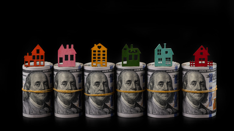 rolls of $100 bills with houses sitting on them