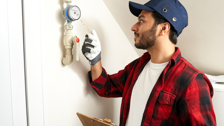 A man holding a paper clip and pen checking a water meter in a home.