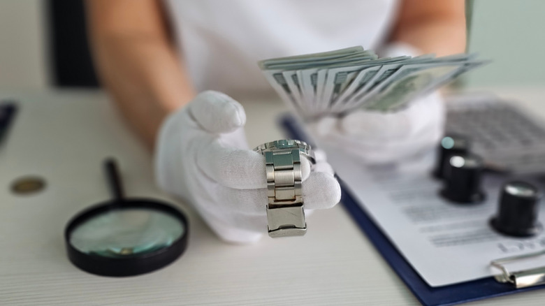 Expert evaluating a luxury watch while counting cash at a transaction site in a well-lit office setting