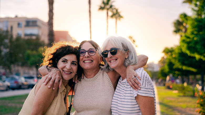Three good friends are embracing and smiling happily on the street at sunset