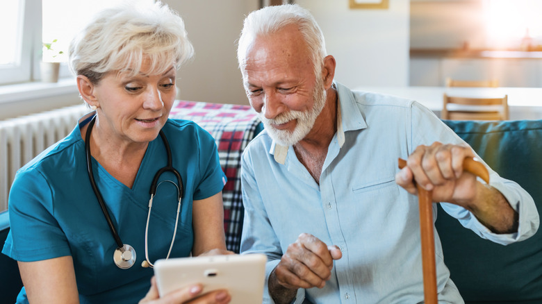 A smiling woman nurse and senior man with a cane using a tablet.