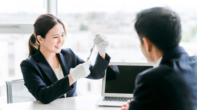 A smiling watch appraiser inspecting a watch while a seller observes.
